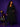 Lady Q’s Corner black longline wool-blend belted coat worn by a model against a purple background.